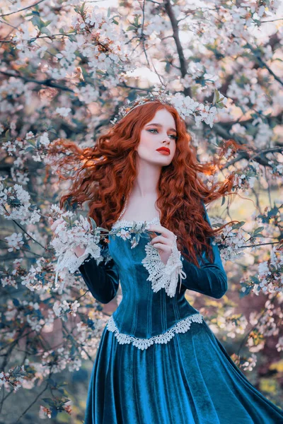 Fantasy ritratto dai capelli rossi ragazza romantica principessa si trova in primavera giardino fiorito. Fioritura fiori di albero verde. Capelli lunghi labbra rosse viso pallido pelle. donna regina medievale vintage creativo design abito — Foto Stock