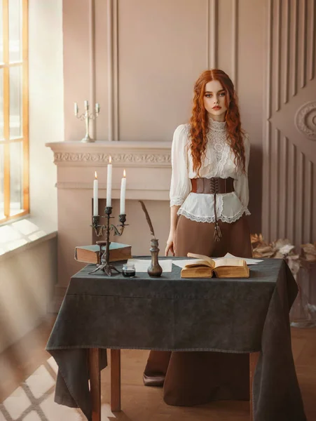 Red-haired woman in vintage dress stands in classic room, window sun light. Clothing costume countess old style white blouse, brown long skirt. Curly red hair. Redhead girl princess looks at camera. — Foto Stock