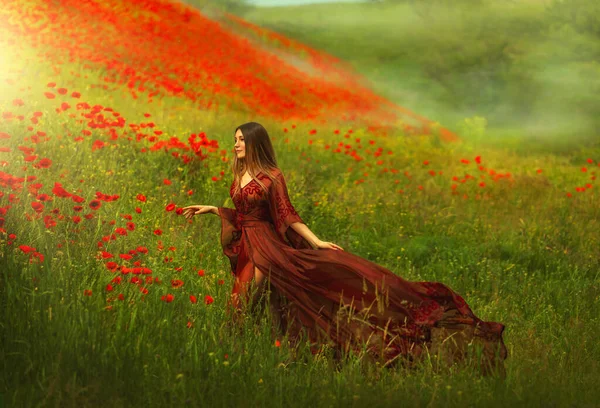 Happy fantasy woman queen in red silk dress, walking in poppy field, summer green grass, nature flowers. Girl goddess princess train hem skirt flying in wind, satin fabric waving. divine sun light