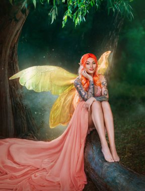 Fantasy art portrait red-haired woman fairy sits on log, creative design costume butterfly wings bright glow. Elf girl in orange peach sexy dress. Night dark forest mystic summer nature green trees.