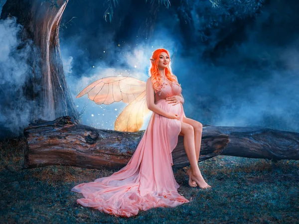 Fantasy art portrait red-haired woman fairy sits on log, creative design costume butterfly wings bright glow. Elf girl in orange peach sexy dress. Night dark forest mystic summer nature green trees.