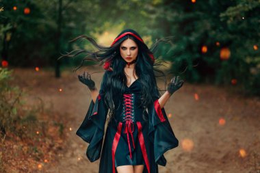 Fantezi kadın cadı sihirli eller oluşturur. Rüzgâr hareketinde uçan uzun saçlar. Seksi yüz, siyah gözler kameraya bakar. Yaz doğası yeşil orman ağaçları. Gotik kız sanatı. Siyah kırmızı elbise. Eski moda.