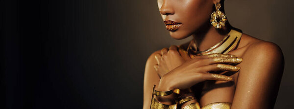 Portrait Closeup shiny golden lip gloss on lips Beauty fantasy African American woman, cropped face in gold paint perfect skin. Fashion model girl goddess. jewellery accessories art metallic makeup