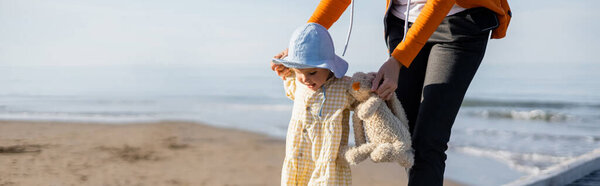Woman holding toddler kid and toy on beach in Treviso, banner 