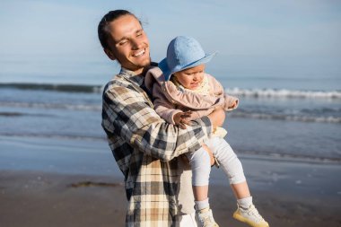 Happy dad holding baby girl near blurred adriatic sea in Italy  clipart