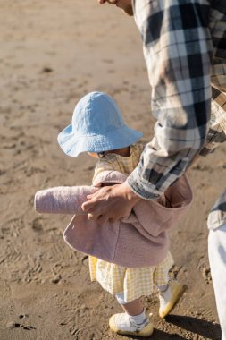 Baba, plajda panama şapkalı küçük bir çocuğa dokunuyor. 