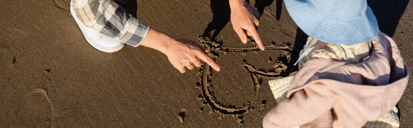 Cropped view of father drawing heart sign on sand near daughter, banner