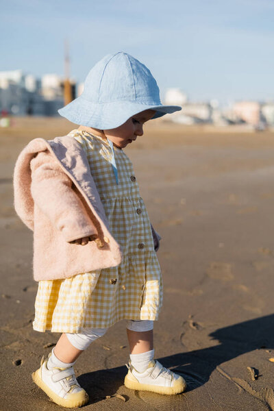 Side view of baby girl in panama hat walking on sandy beach 