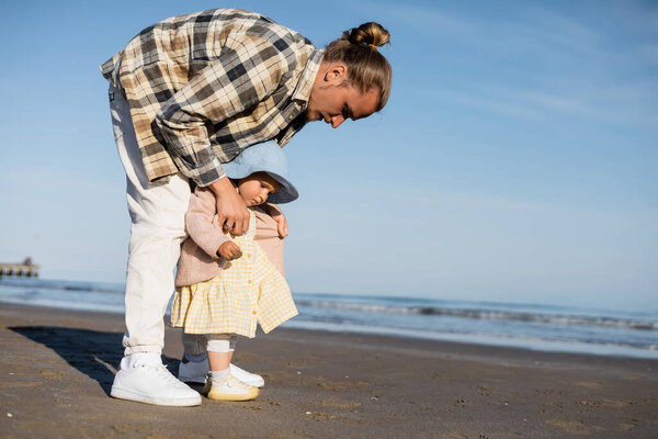 Young man wearing jacket on baby girl on beach near adriatic sea in Italy 