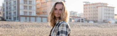 Young long haired man standing on beach in Italy, banner  clipart