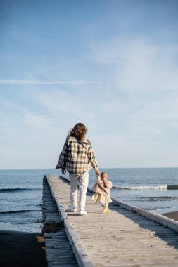 Back view of father and baby girl walking on pier near adriatic sea in Italy  clipart