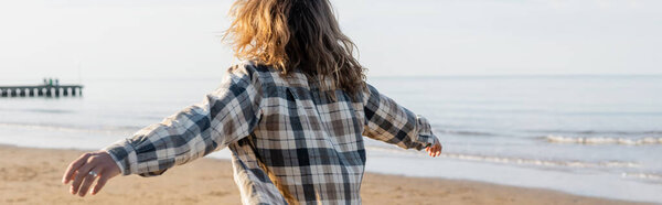 Back view of long haired man in shirt walking on beach near adriatic sea in Italy, banner 