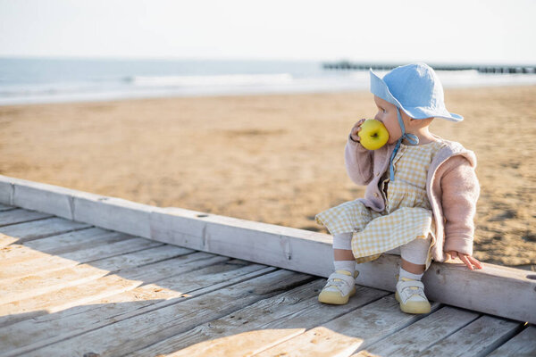 Side view of toddler child eating apple on wooden pier in Italy 