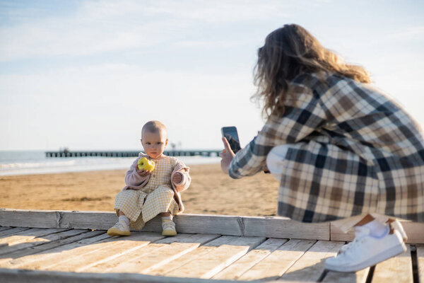 Blurred man taking photo of baby girl with apple on pier in Italy 