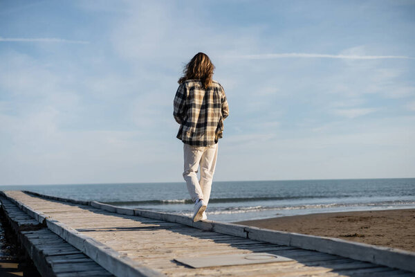 Back view of long haired man walking on wooden pier near adriatic sea in Italy 