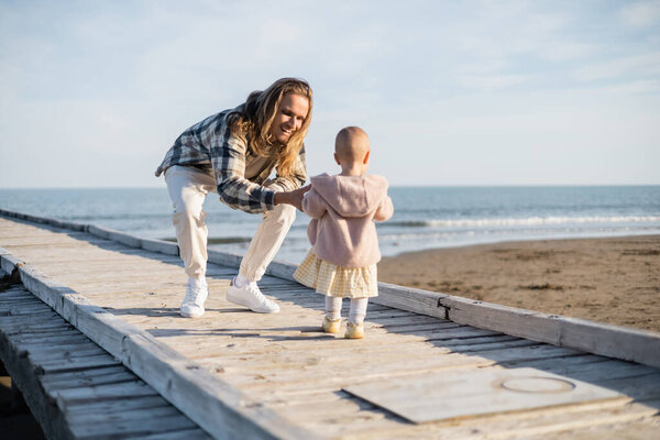 Positive man in shirt looking away baby on wooden pier in Italy 