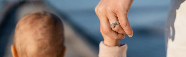 Cropped view of man holding hand of toddler daughter near sea, banner 