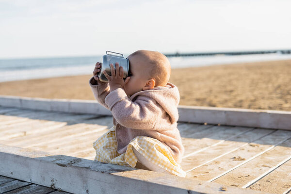 Baby girl drinking from cup on beach in Italy 