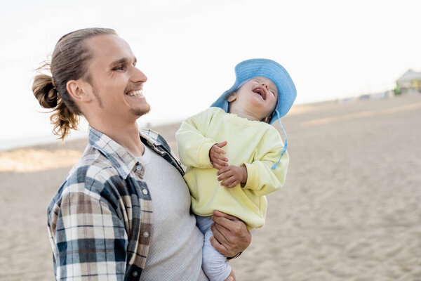 Positive dad and toddler daughter spending time on beach 