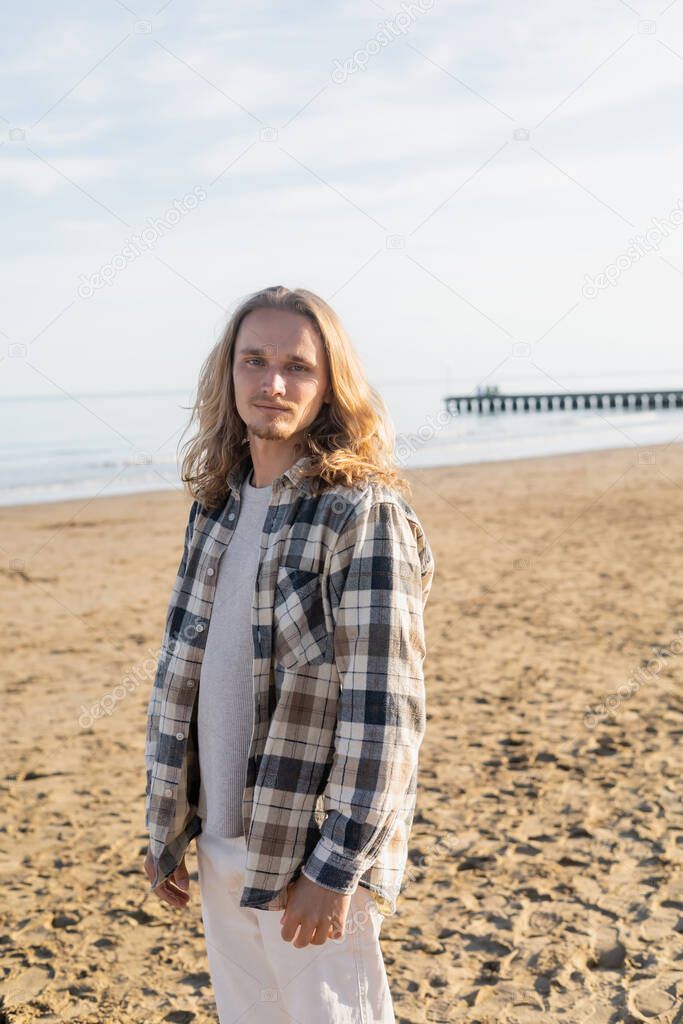 Long haired man in shirt looking at camera on beach in Italy 