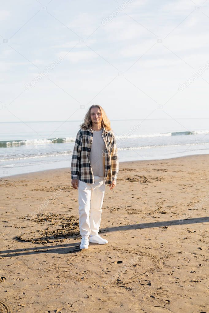 Smiling man in checkered shirt standing on beach near adriatic sea in Italy 