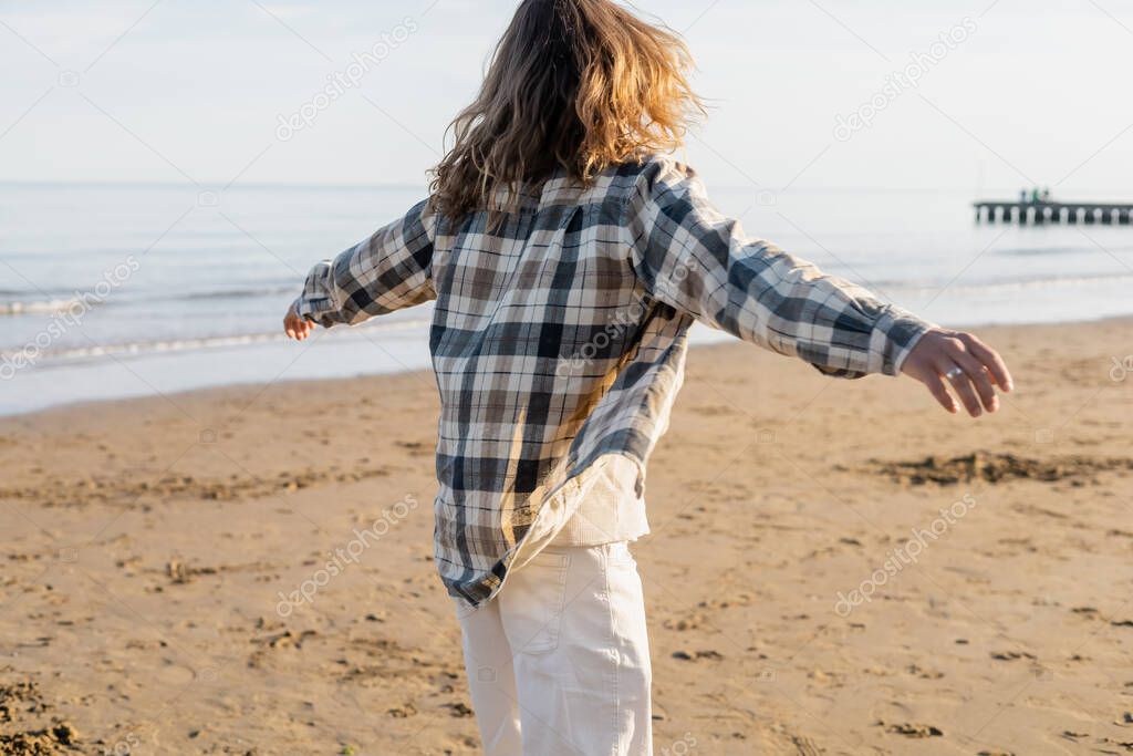 Back view of long haired man in checkered shirt walking on beach in Treviso