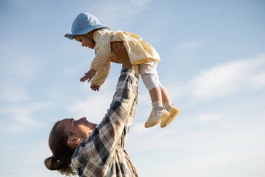 Arka planda gökyüzü olan küçük kızını kucağında tutan genç babanın yan görüntüsü 