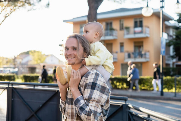 Счастливый молодой человек с ребенком на плечах на городской улице в Тревизо