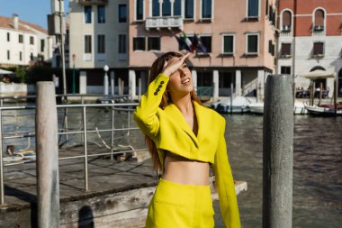 young woman in yellow suit holding hand above eyes and looking away in Venice clipart