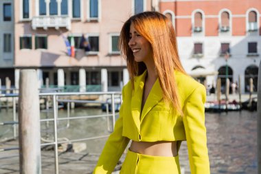 Venedik 'teki bulanık arka planda gülümseyen sarı elbiseli mutlu kızıl kadın.