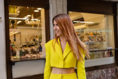 Venedik 'te dükkanları olan, binanın yakınında gülümseyen sarı elbiseli şık kızıl saçlı kadın.