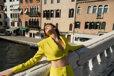 Sarı elbiseli kadın Venedik 'teki köprüde gözleri kapalı dinleniyor.