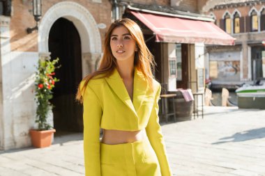 Venedik 'teki bulanık sokakta gülümseyen şık sarı takım elbiseli genç kızıl saçlı kadın.