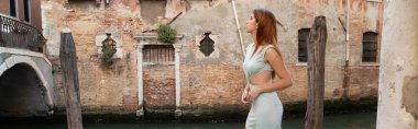Venedik 'teki ortaçağ binasına bakan zarif elbiseli kızıl saçlı kadının yan görüntüsü.