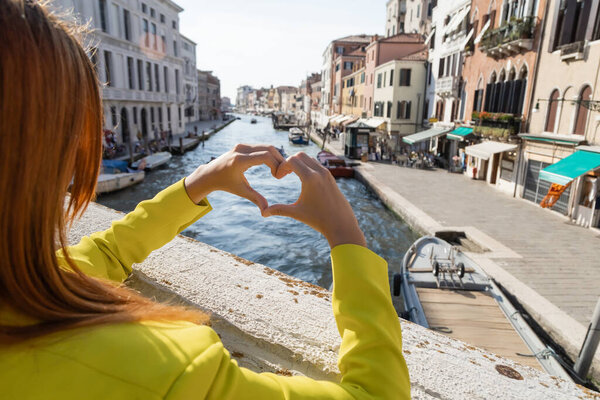 partial view of redhead woman showing heart sign over blurred Grand Canal in Venice
