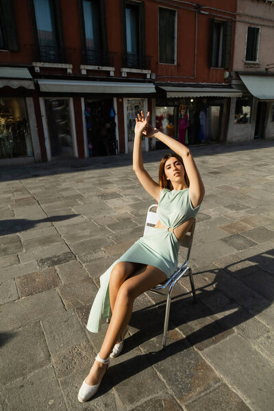 full length of woman in elegant dress sitting on chair on street in Venice