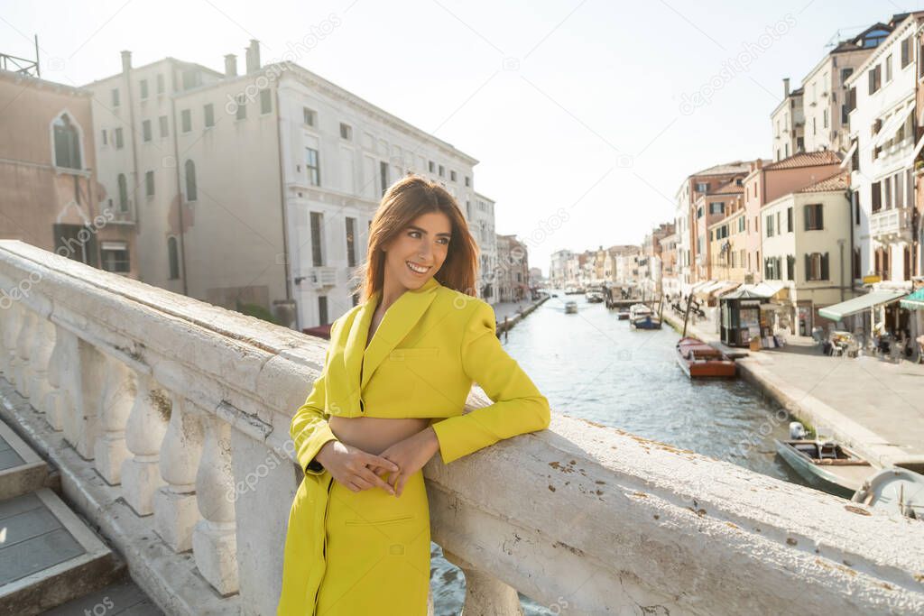 redhead woman in yellow suit smiling on bridge over Grand Canal in Venice