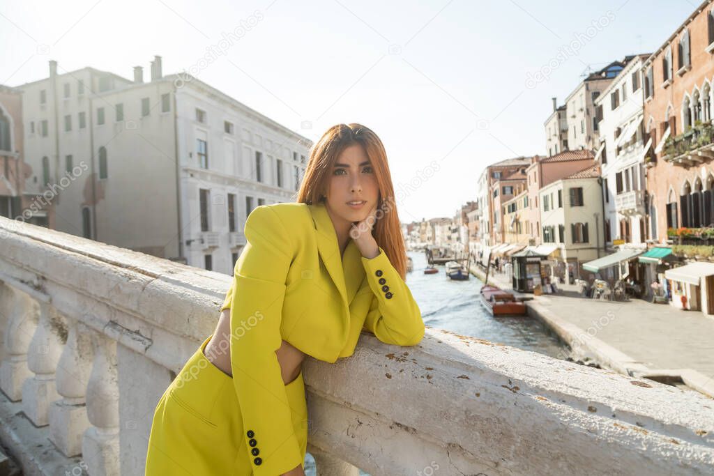 trendy redhead woman looking at camera while standing on bridge over venetian Grand Canal