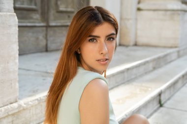 Venedik 'teki bulanık sokakta kameraya bakan çekici kızıl saçlı kadının portresi.