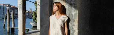 Venedik 'te taş duvarın yanındaki Grand Canal' a kolsuz kazaklı genç bir kadın bakıyor.
