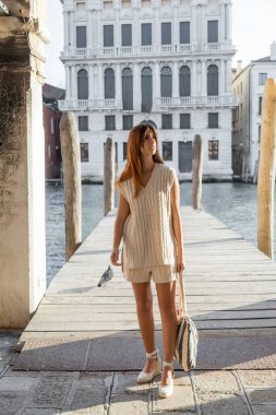 Venedik 'teki ahşap iskelenin yanından uzaklaşan çizgili çantalı bir kadın.