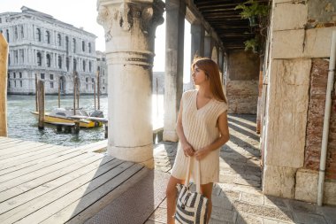 Venedik 'te sütunların yanında duran çizgili çantalı genç kadın Büyük Kanal' a bakıyor.