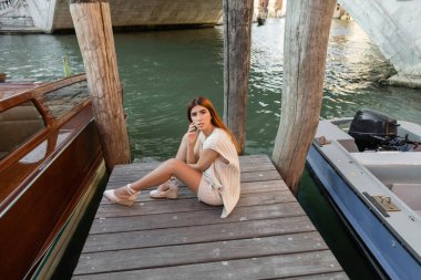 Venedik 'teki ahşap iskelede oturan yüksek açılı örgü elbiseli bir kadın.