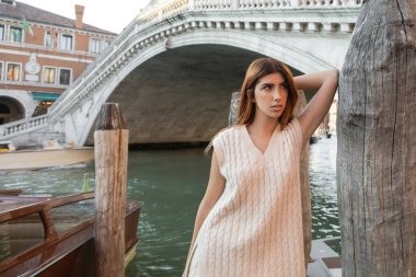 woman in sleeveless shirt leaning on wooden piling near venetian bridge on background clipart