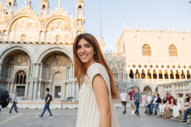 İtalya, Venedik - 12 Mayıs 2022: Venedik 'teki St. Mark Meydanı' nda kameraya bakan mutlu kızıl kadın