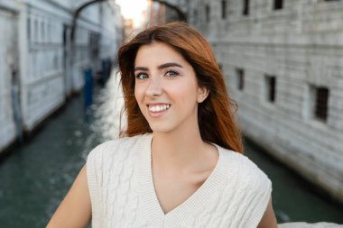 Venedik 'teki bulanık arkaplanda kameraya gülümseyen kızıl saçlı mutlu genç bir kadının portresi.