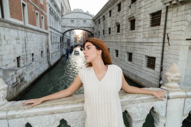 redhead woman looking away near Sighs Bridge on background in Venice clipart