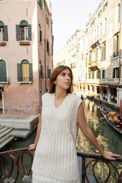 pretty young woman standing near fence over canal in Venice and looking away