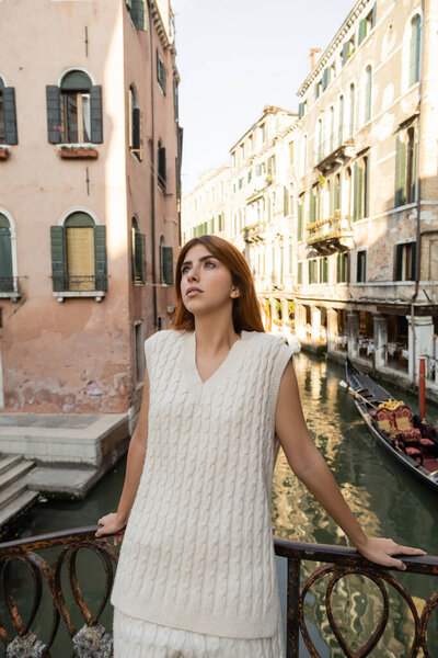 dreamy woman in summer knitwear standing over canal near medieval venetian buildings