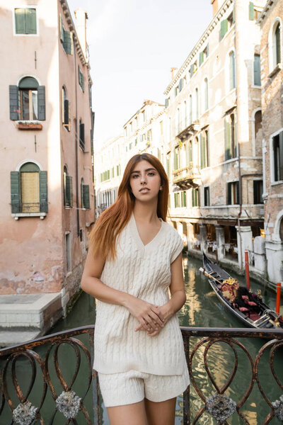 woman in sleeveless jumper looking at camera near fence over venetian canal